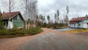 The picture shows two houses. A road runs between the houses.
